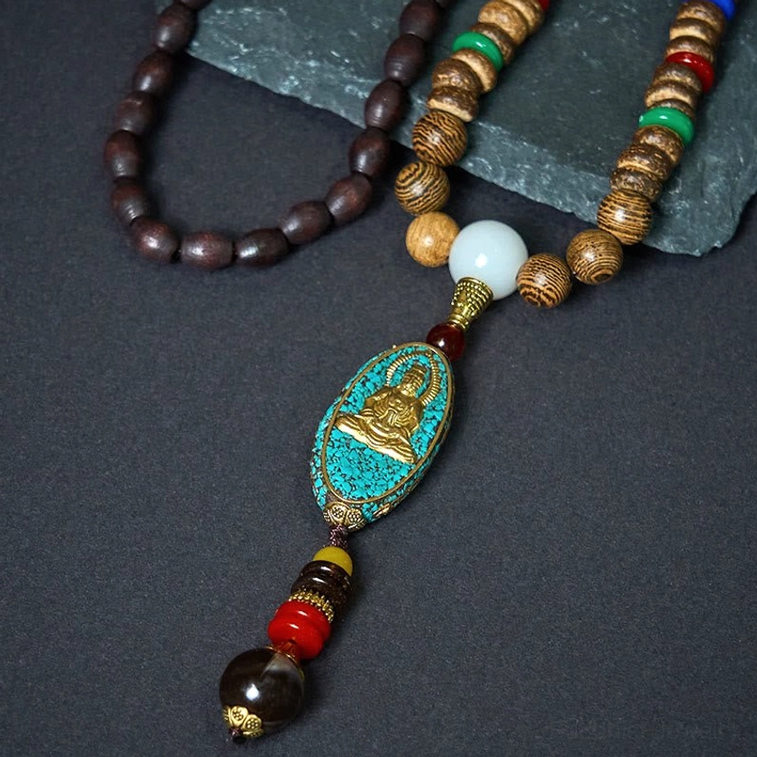 Buddhist mala necklace flat lay on stone slab featuring dark wooden beads, white accent bead and turquoise Avalokitesvara pendant