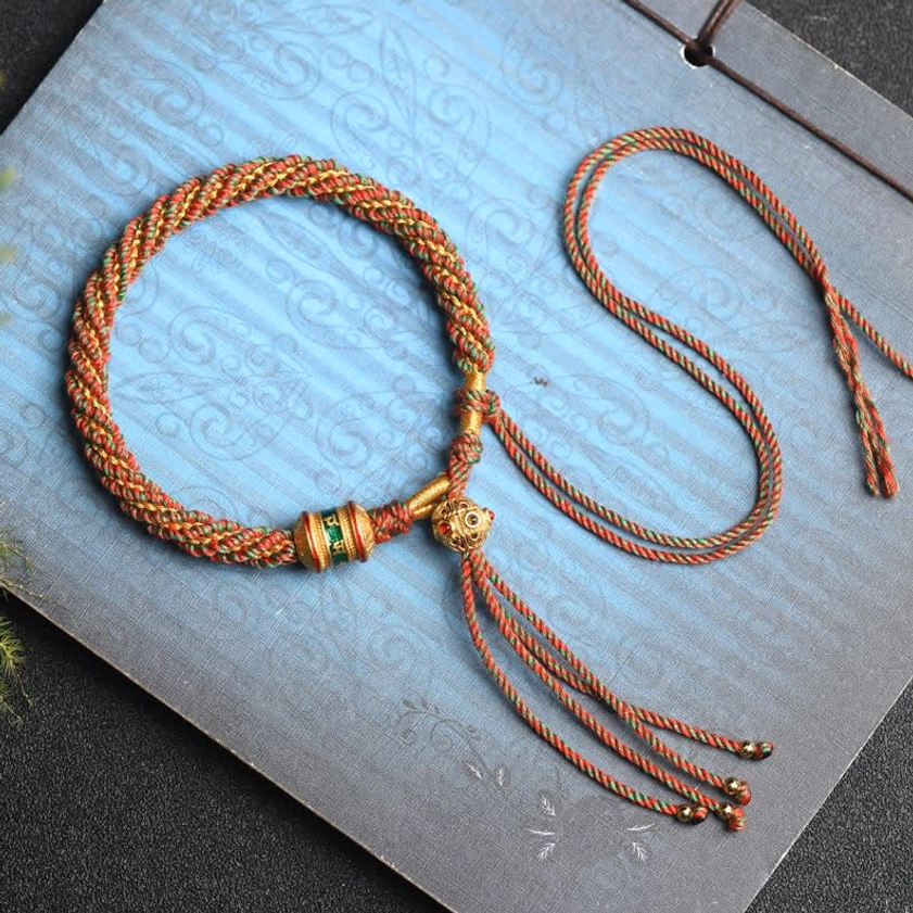 Buddhist prayer wheel charm bracelet flat lay with gold metal hardware and adjustable beaded tassels on vintage backdrop