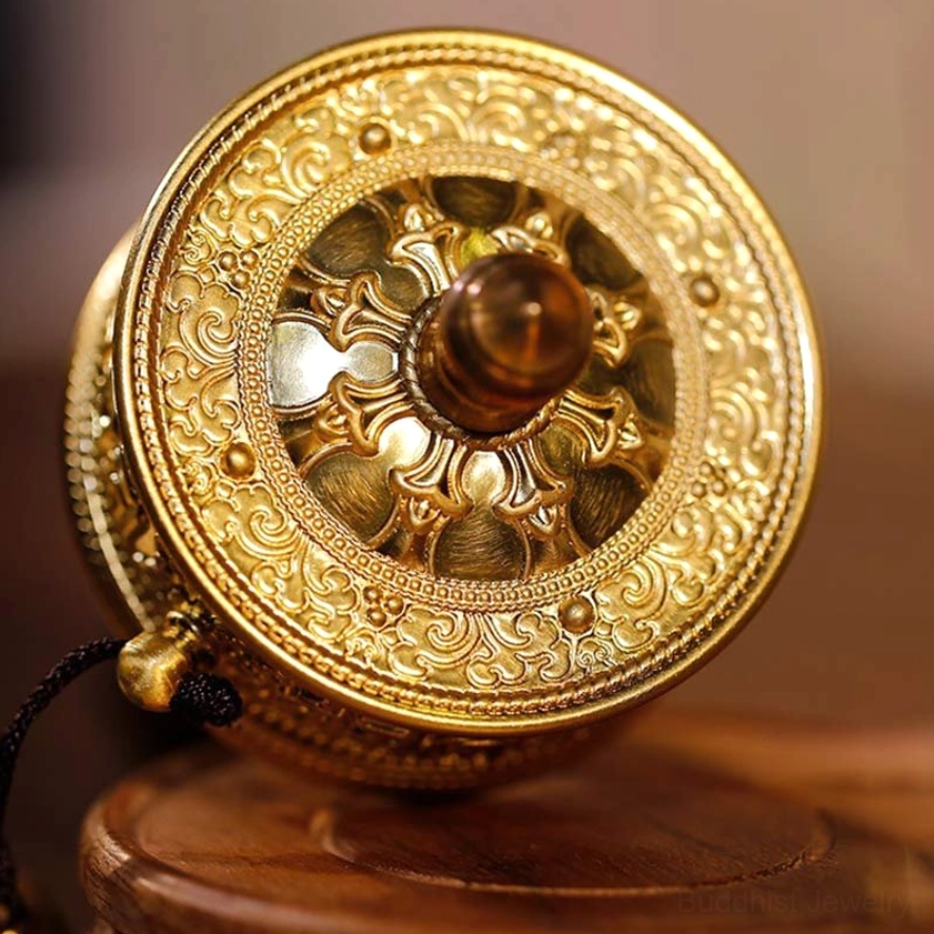 Buddhist prayer wheel end cover with intricate gilt carved patterns and hanging decorative spiritual cord, front close-up showing handcrafted details