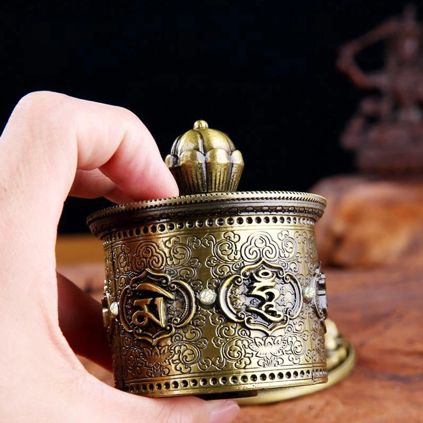 Close-up side view of Buddhist prayer wheel showing intricate mantra emblem plaques and delicate scrollwork details
