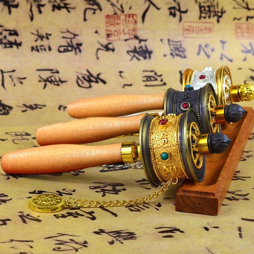 Multiple handcrafted Buddhist prayer wheels with wooden handles displayed from overhead angle, showing intricate metal work and gemstone inlays