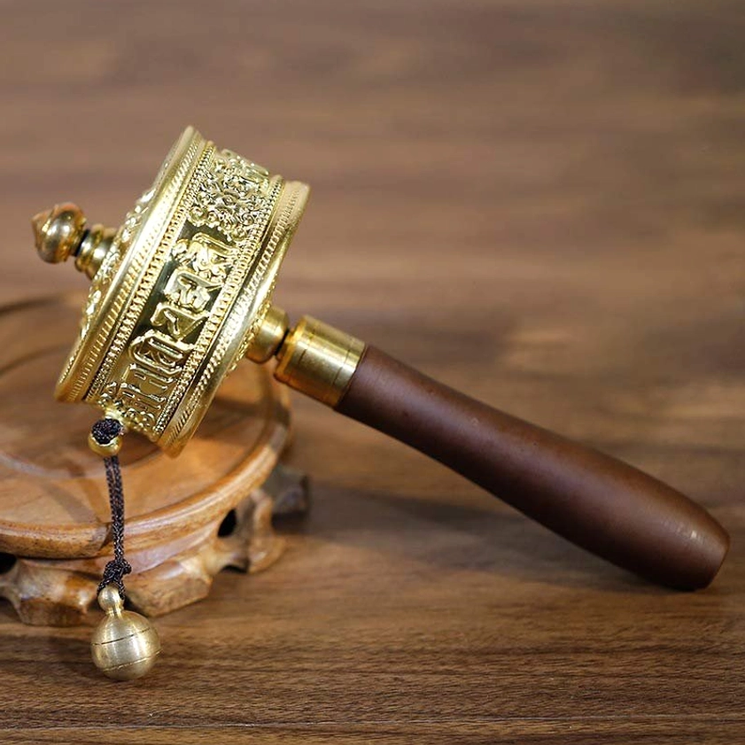 Handmade Buddhist prayer wheel with Om Mani Padme Hum mantra, gilt metal body with engraved Buddhist patterns, dark sandalwood handle, and hanging bell ornament - side view
