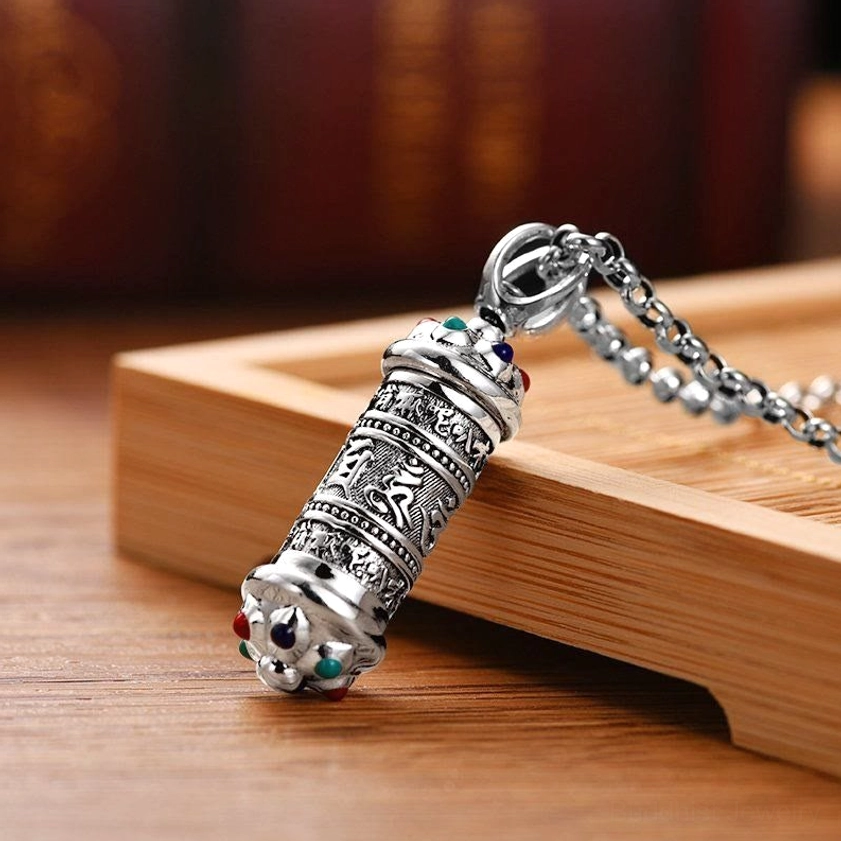 Prayer wheel Buddhist pendant detail showing aged silver finish, engraved Tibetan script, and colored gem decorations