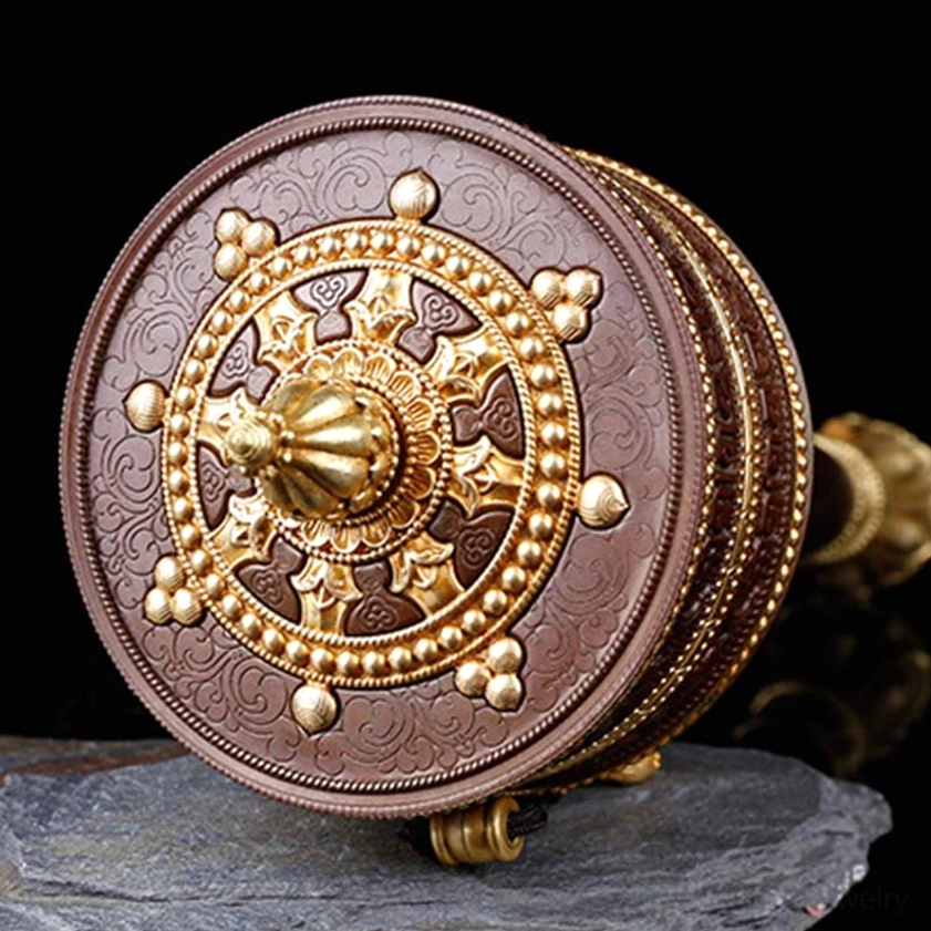 Top-down view of Buddhist prayer wheel drum showing gilded Dharma wheel pattern and embossed sacred text on slate