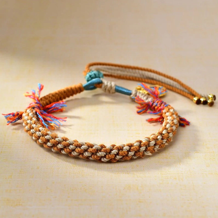 Flat lay view of adjustable Buddhist string bracelet with dual colorful tassel sets, braided rope construction, gold-plated drawstring beads, and protective Zakiram goddess pendant