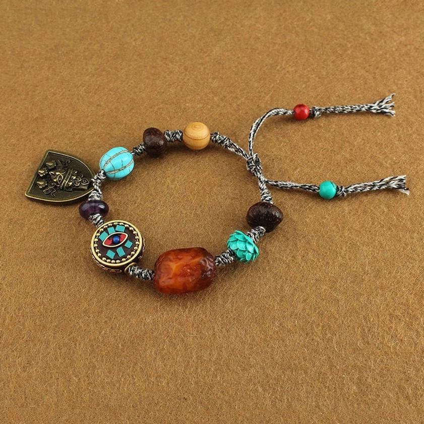 Buddhist protection bracelet detail shot showing adjustable braided tassel ends, mixed gemstone beads, and vintage metal pendant
