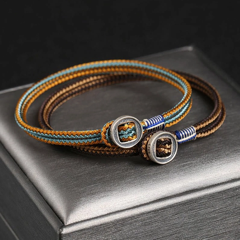 Top-down view of dual-strand handmade silver Buddhist bracelet with brown yellow blue woven pattern and decorative metal buckles