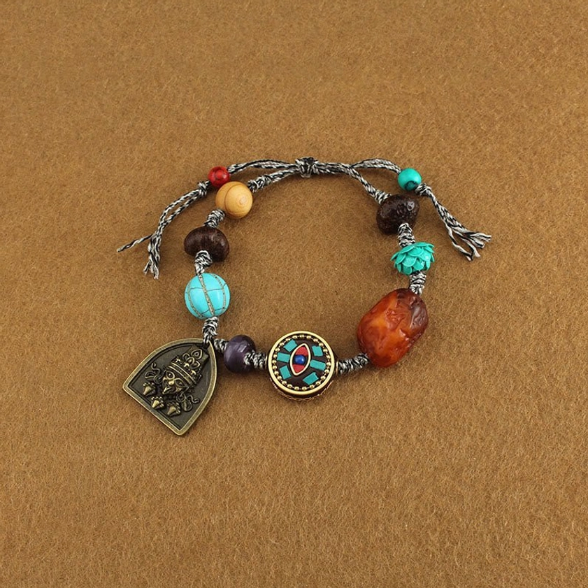 Flat lay overhead view of handmade Buddhist protection rope bracelet featuring enamel round bead, amber stone, and vintage metal charm