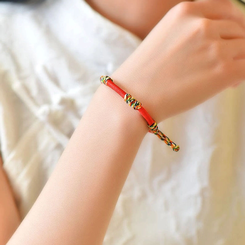 Red Buddhist bracelet on forearm showing wearing comfort and design with colorful woven knot accents