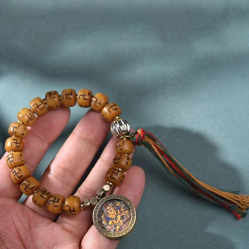 Buddhist protection bracelet held in hand showing camel bone beads, round Buddha amulet, and woven tassel clarity