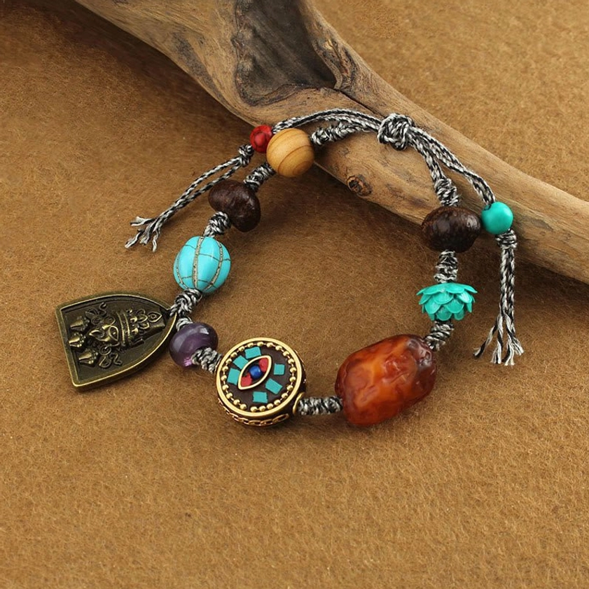 Side angle view of Buddhist protection bracelet with turquoise lotus bead, enamel charm, wooden and stone beads on rustic backdrop