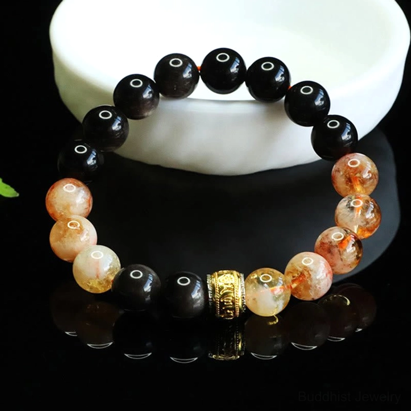 Sacred mantra bracelet with polished black obsidian and golden citrine beads on white ceramic tray, showing craftsmanship detail