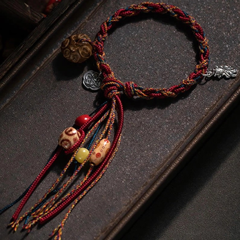 Handmade Buddhist red string bracelet top-down flat lay showing multicolor braided cords, sterling silver charms, mixed decorative beads and long tassel