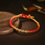 Red and gold handwoven Buddhist protection bracelet with dragon scale knot, adjustable sliding clasp on dark background
