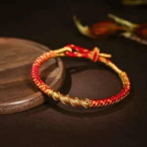 Red and gold handwoven Buddhist protection bracelet with dragon scale knot, adjustable sliding clasp on dark background