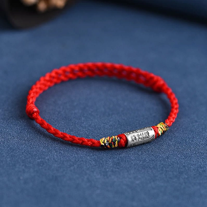 Side three-quarter view of handcrafted Buddhist protection bracelet showing silver ornament attached to braided cotton rope, dark background