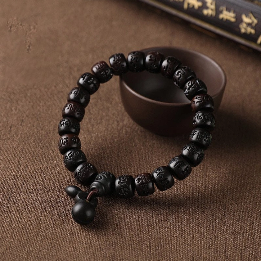 Single Buddhist mala wooden bracelet with black carved meditation beads and round wooden pendant charm on brown fabric