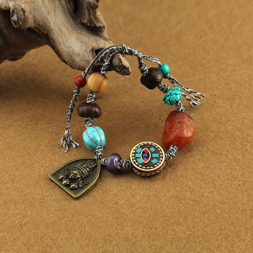 Buddhist protection bracelet with turquoise lotus bead and deity charm on brown fabric background, showing detailed braided rope and mixed gemstone beads