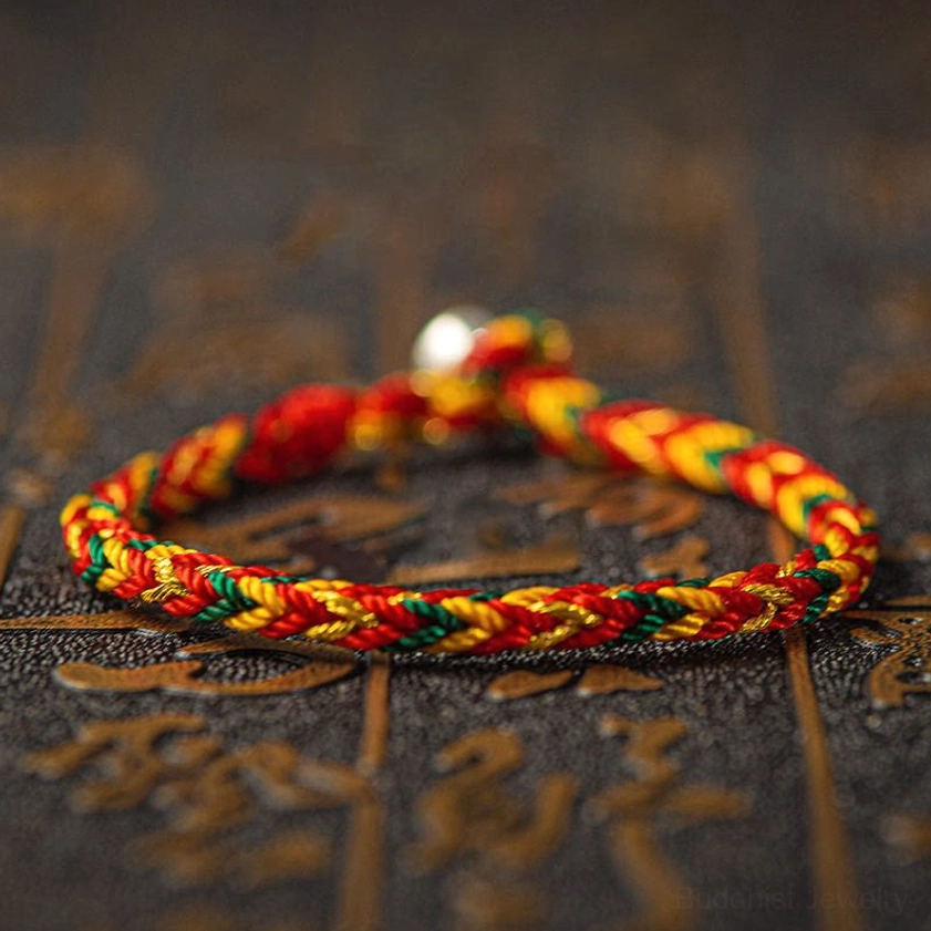 Vibrant multicolored Buddhist string bracelet with red yellow green blue woven threads and silver bead clasp on sacred dark background