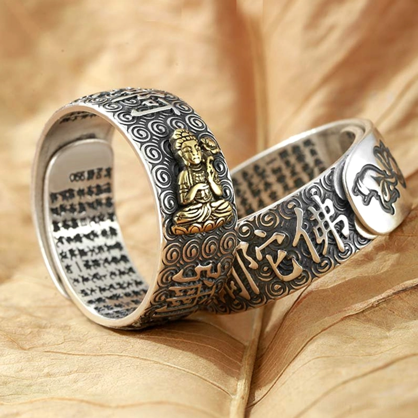 Buddhist protective copper ring with engraved Namo Buddha text and gold Buddha ornament, pair display on dry leaf background showing sutra detail inside band