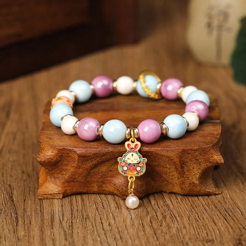 Single Buddhist protection bracelet featuring rabbit enamel charm and pastel porcelain beads on wooden display stand