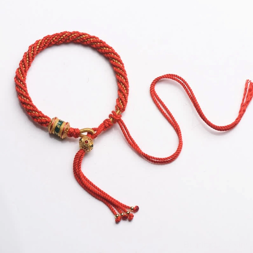 Bright red Buddhist prayer wheel braided bracelet overhead view with gold metal charms and beaded tassel ends