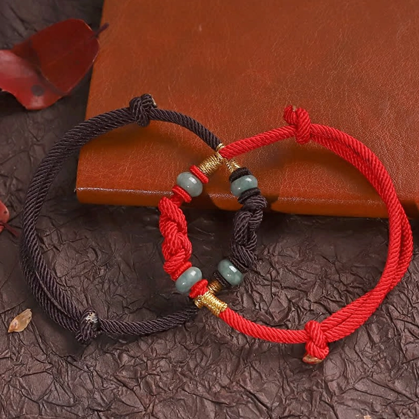 Red and dark brown jade bracelets with adjustable pull knots and gold accents on leather notebook setting