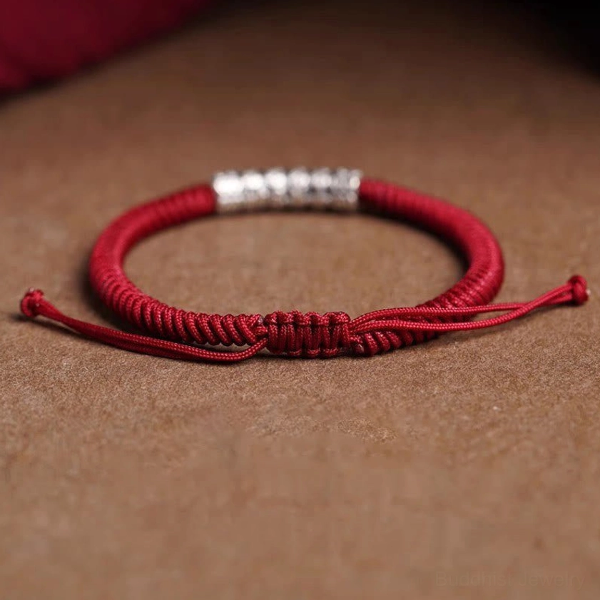 Flat lay of adjustable dark red Buddhist rope bracelet with sterling silver bead on wooden surface