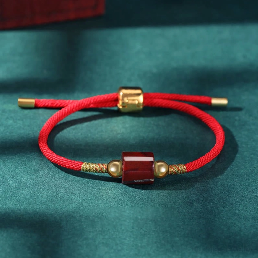 Red stone Buddhist bracelet with red braided rope and gold metal accents for luck and protection