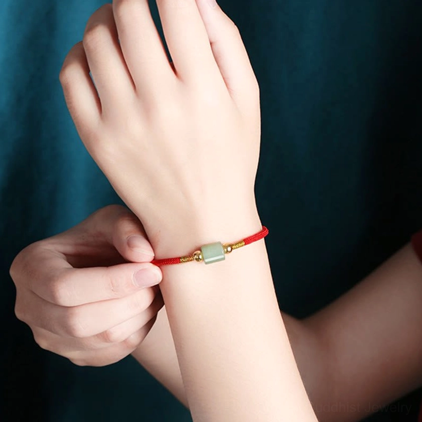 Hands adjusting Buddhist bracelet showing flexible red rope with green aventurine bead and gold sliding clasp mechanism