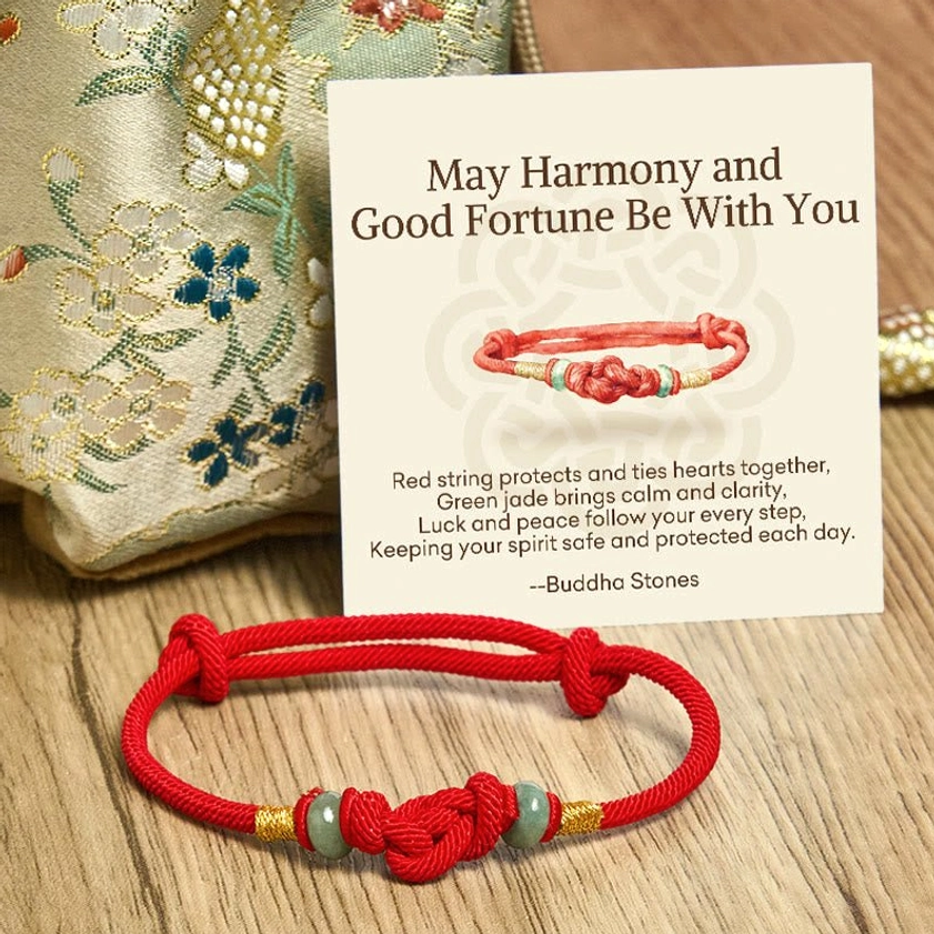 Red string jade Buddhist protection bracelet and blessing card arranged on embroidered silk fabric wooden surface