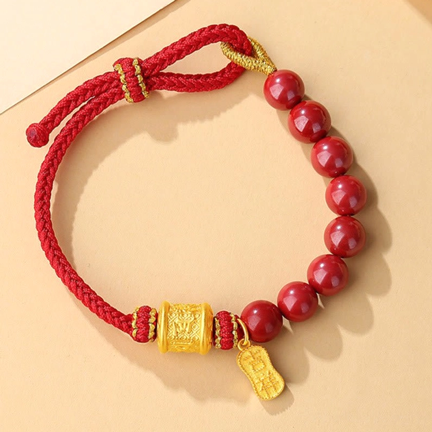 Single-strand red string cinnabar bracelet with gold accents - side angle flat lay