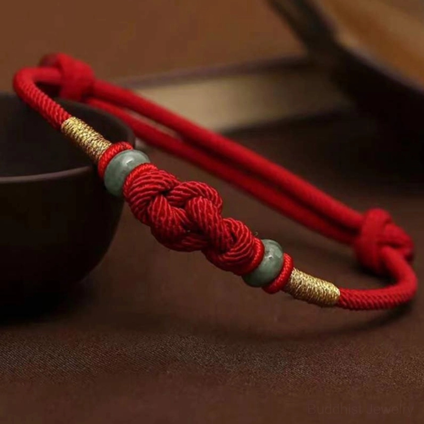 Close-up side view of red string jade Buddhist bracelet showing intricate braided knot, green jade beads, and gold accents in ceramic bowl setting