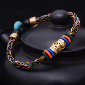 Handmade Buddhist red string bracelet with copper coin and eight knots, displayed on black teapot showing multicolor braided design with gold accents