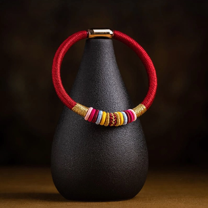 Handmade Buddhist red string bracelet displayed on ceramic stand with wooden tabletop
