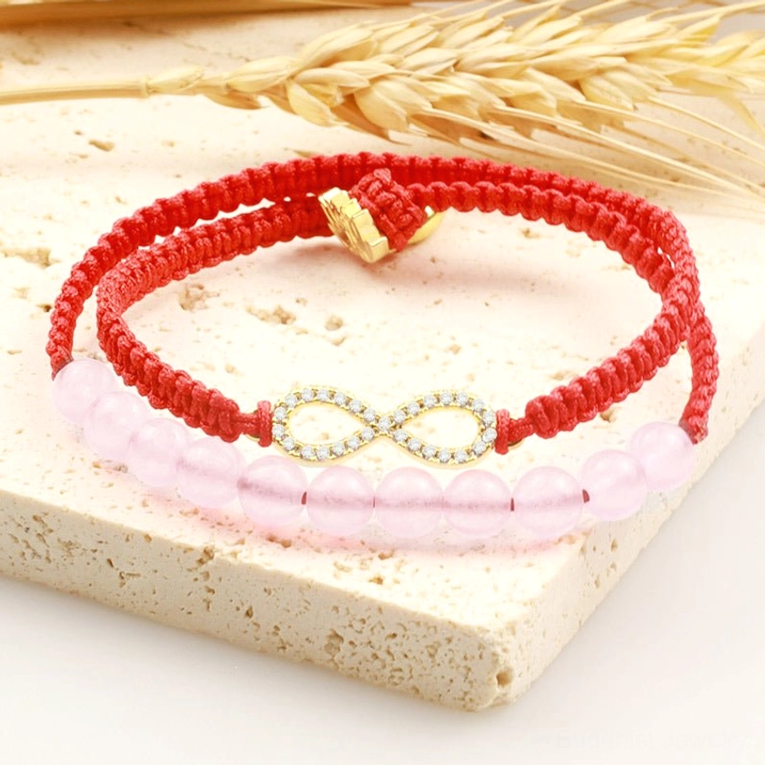 Red string pink crystal bracelet flat lay on natural stone tray with gold lotus charm detail and woven red cord