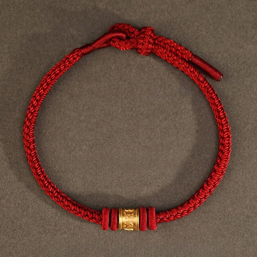 Full view of adjustable red cord protection bracelet with central gold mantra bead, flat lay perspective