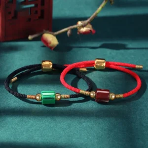 Dual style green aventurine and malachite handmade Buddhist red string bracelets with gold hardware displayed on decorative Chinese desktop