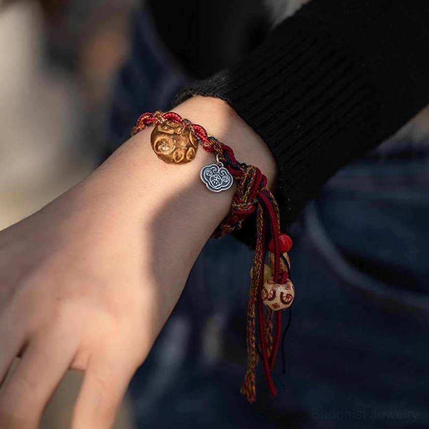 Handmade Buddhist string bracelet on hand displaying red cord, sterling silver koi fish and Ruyi charms, casual daily wear styling