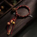 Handmade Buddhist red string bracelet with 925 sterling silver koi fish charm, multicolor braided cord with Bodhi seed beads and tassel, flat lay on dark wooden surface