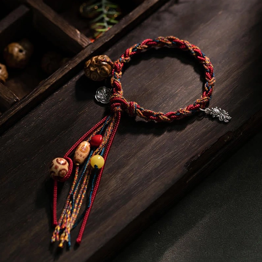 Handmade Buddhist red string bracelet with 925 sterling silver koi fish charm, multicolor braided cord with Bodhi seed beads and tassel, flat lay on dark wooden surface