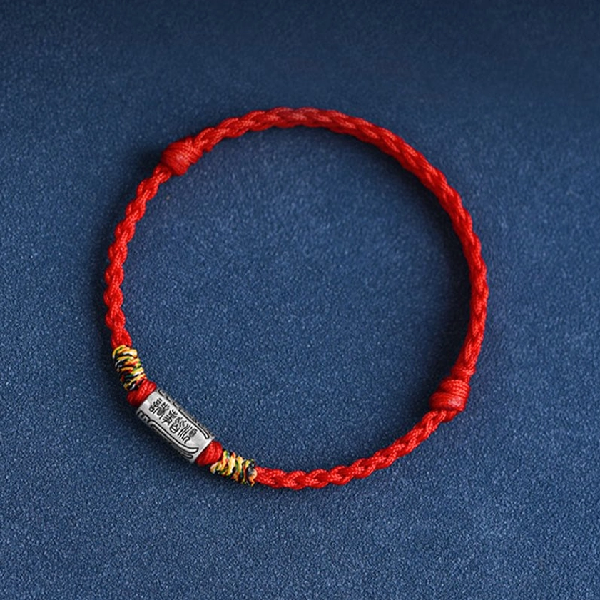 Minimalist Buddhist bracelet with red braided rope and sterling silver engraved charm, front view showing detailed metalwork on dark backdrop