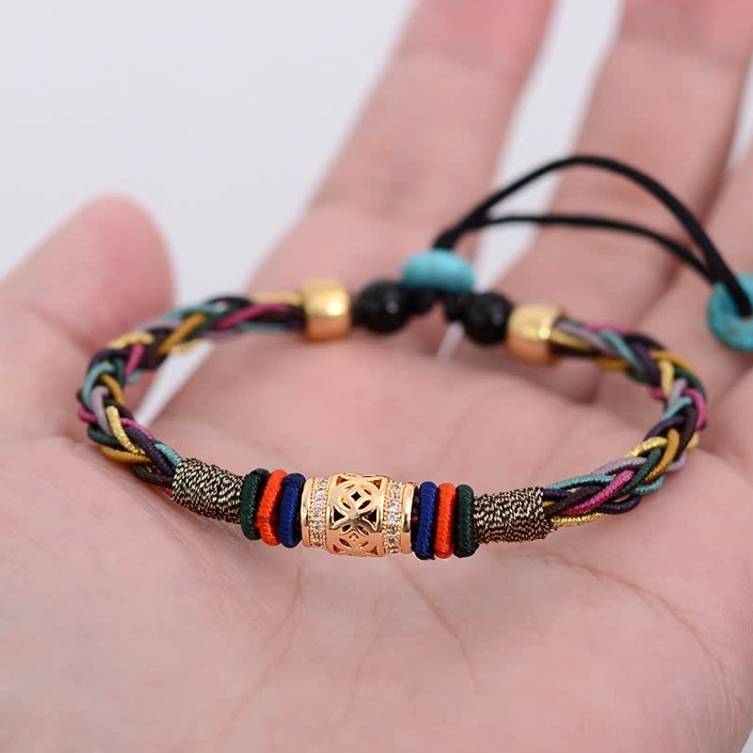 Buddhist red string bracelet held in palm of hand showing colorful braided rope with dual metal decorative beads and adjustable closure