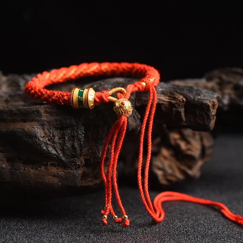Solid red Buddhist lucky string bracelet with prayer wheel bead and gold green metal charms on wooden surface