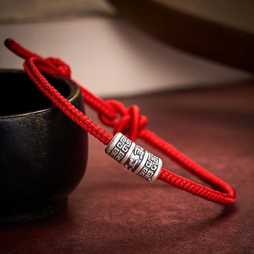 Handmade Buddhist red string protection bracelet with adjustable knot, side view showcasing engraved silver mantra bead detail