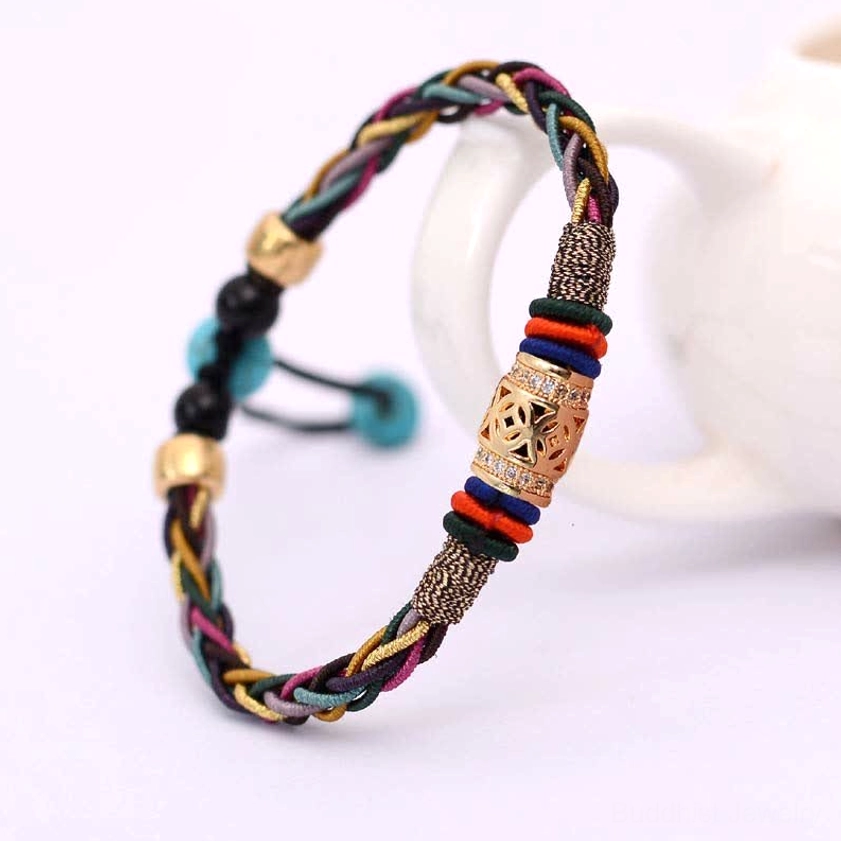 Side view of handmade Buddhist red string bracelet with adjustable pull cord and carved metal cylindrical bead on white ceramic backdrop