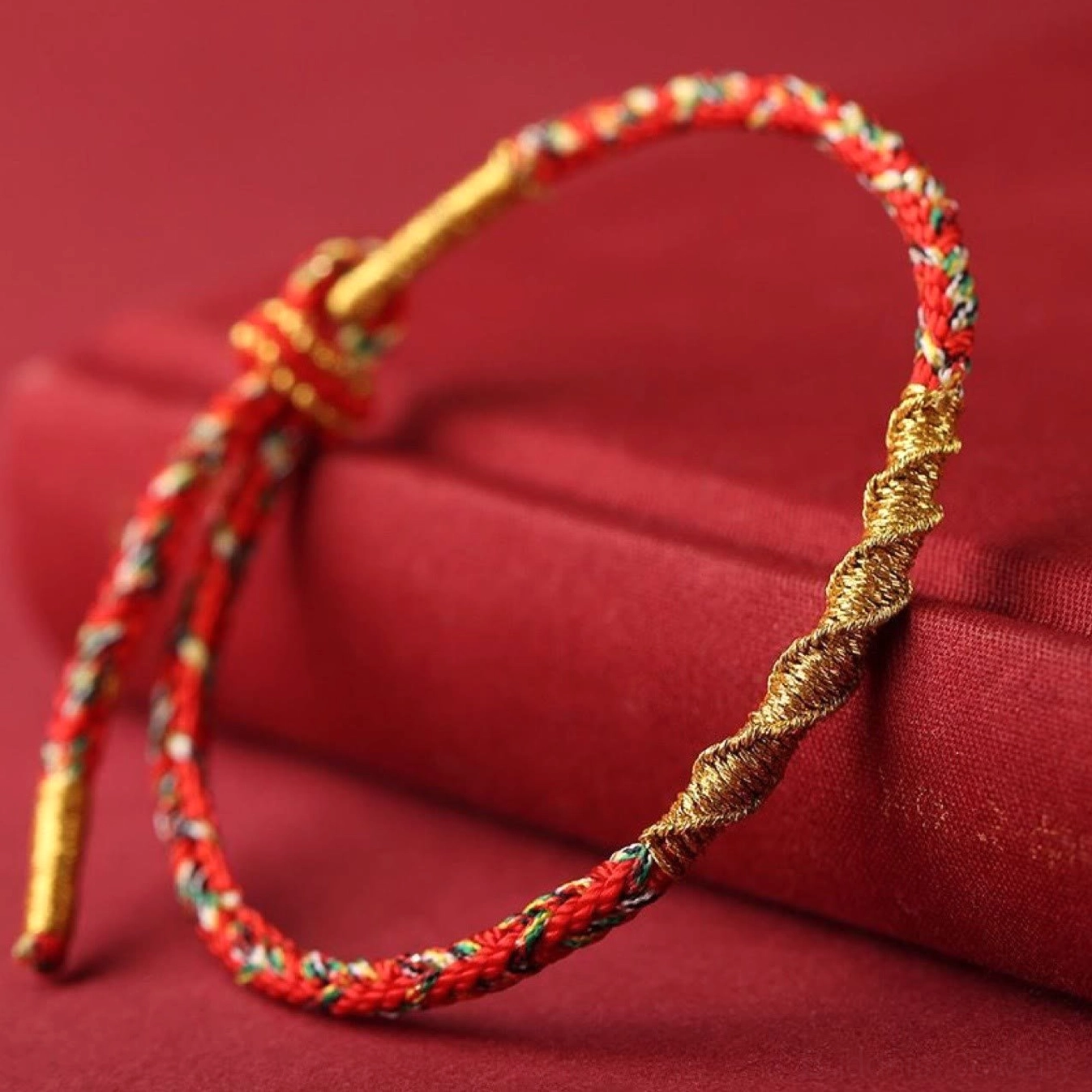Red and gold Buddhist red string bracelet on fabric surface showing adjustable braided knot fastener detail