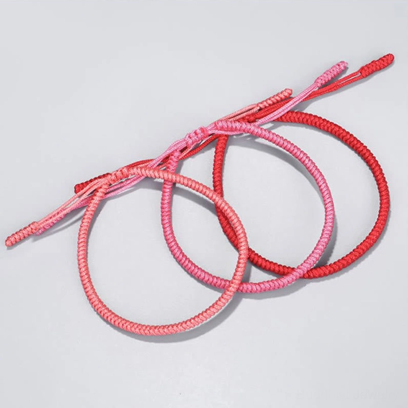 Three handmade Buddhist red string bracelets in red, light pink, and dark red tones, showing simple woven braided texture