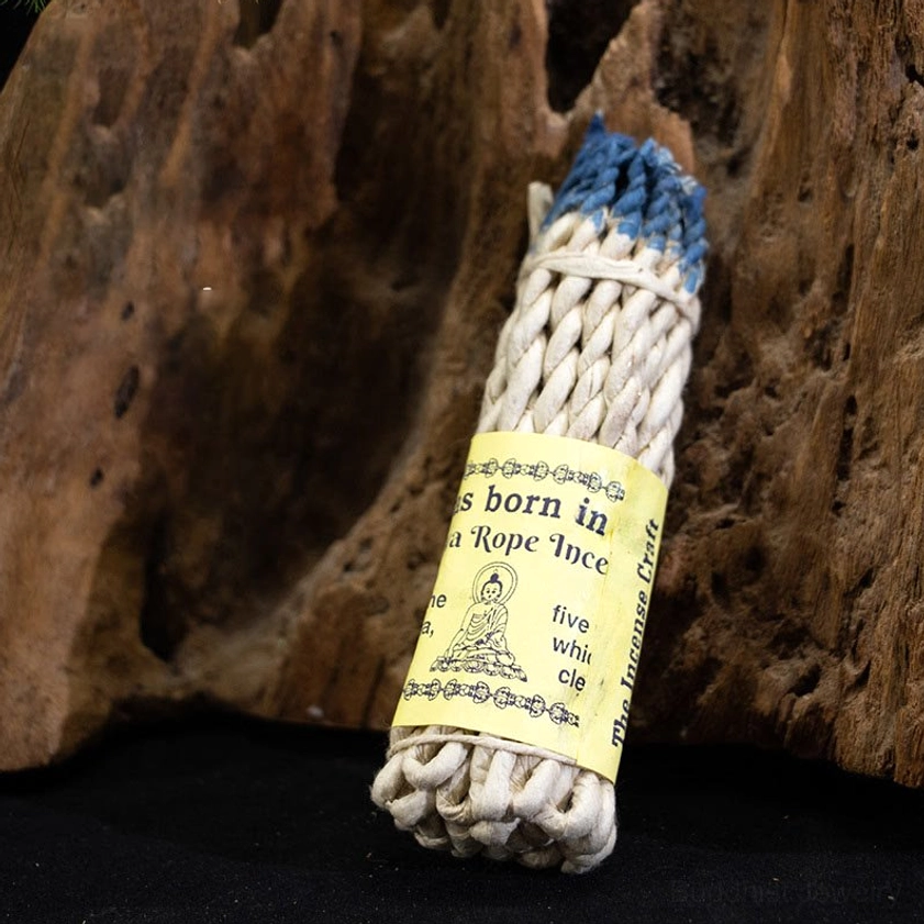 Buddhist rope incense stick with blue-dyed top ends and twisted woven design on wooden background, featuring printed label showcasing traditional spiritual craftsmanship