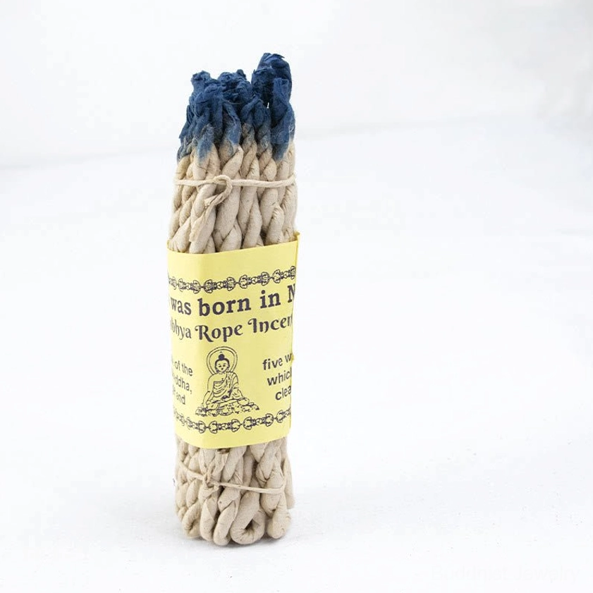 Single Buddhist rope incense bundle with blue-dyed top tips showing thick twisted woven texture and handmade paper tag with Buddha illustration, ideal for meditation